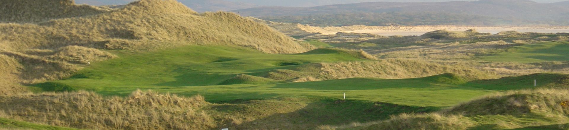 Immerse yourself in the breathtaking landscape of Sandy Hills Links at Rosapenna Golf Resort. A pristine golf course surrounded by rolling green hills showcasing natural beauty and challenging play.